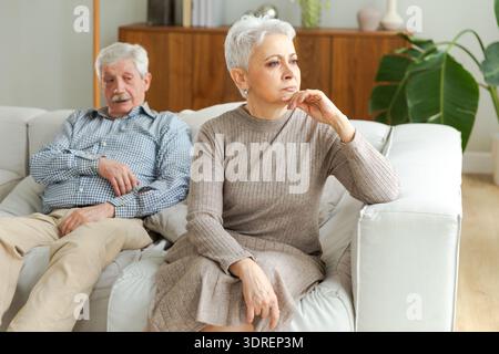 Marriage crisis relationship problems. Old couple quarreling. Sad mature disappointed woman sitting away from husband after havi Stock Photo