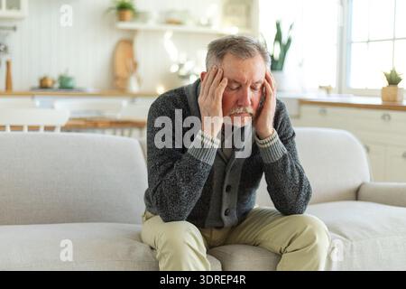 Headache pain. Unhappy middle aged senior man suffering from headache sick rubbing temples at home. Mature old senior grandfathe Stock Photo