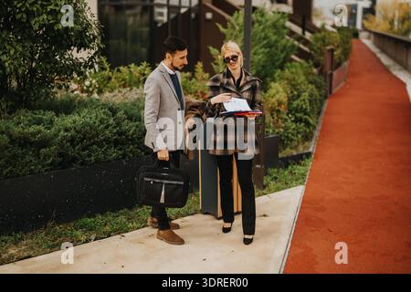 Business professionals outside office discuss documents, smiling as they review files on a sunny day Stock Photo