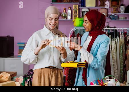 Two women wearing hijabs are smiling while shopping for new sunglasses and discussing fashion trends together in a retail boutique, enjoying their fri Stock Photo