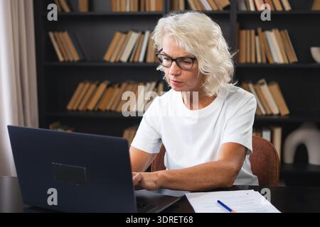 Confident stylish middle aged senior woman using laptop at workplace. Older mature lady businesswoman sitting at office table wi Stock Photo