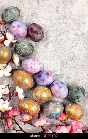 Marble Easter eggs, dyed with golden turmeric and hibiscus tea on a gray concrete background with sakura branches, ideas for hom Stock Photo