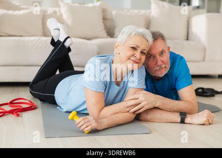 Fitness workout home training. Senior adult mature healthy fit couple resting after sports exercise on yoga mat at home. Mid age Stock Photo