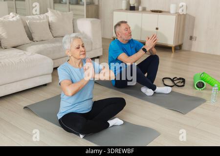 Yoga mindfulness meditation. Senior adult mature couple practicing yoga at home. Mid age old husband wife sitting in lotus pose Stock Photo