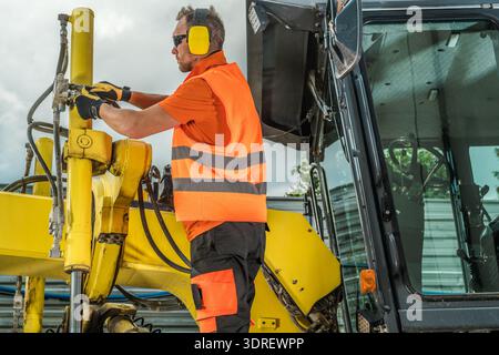 A construction worker in safety gear uses equipment on a project site. Clouds are visible above. Stock Photo