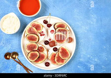 Ricotta,figs and bruschetta with honey on blue marble.Fresh sandwiches and toast with cream cheese,sliced figs,honey and cherrie Stock Photo