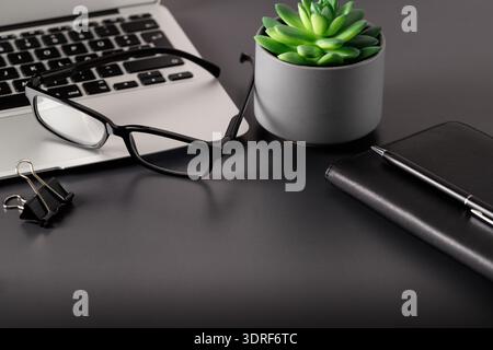 Minimal workplace with laptop, notepad,  small succulent and accessories on a dark grey background. Selective focus Stock Photo