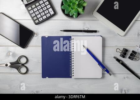 Minimal  unisex workplace with tablet, open blue notepad, smartphone, small succulent and accessories on light grey wooden background. Stock Photo