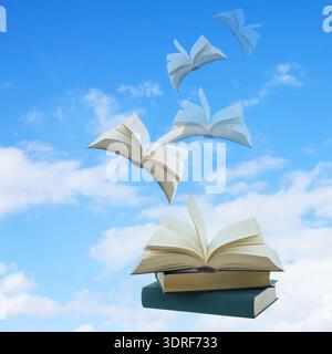 Flying pile of books on blue background with copy space. Open books flying into sky with clouds. Stock Photo