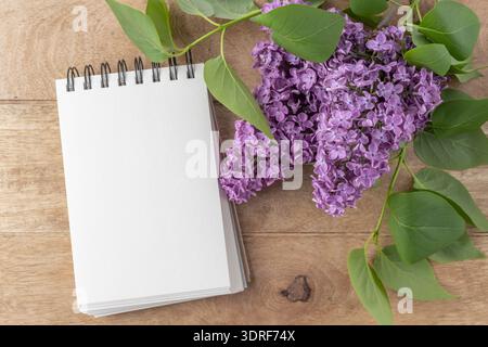 Lilac flowers and open blank notebook scrapbook on rustic wooden background. Top view floral mockup card in vintage style with copy space. Stock Photo