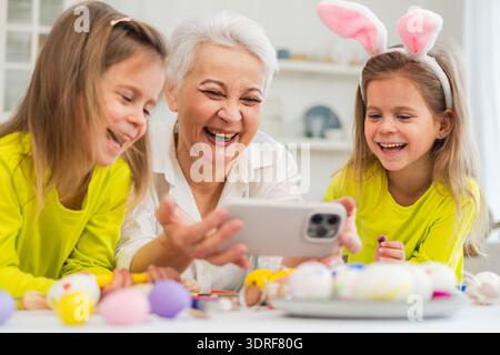 Happy Easter. Two girls sisters twins grandmother painting eggs watching video on phone enjoying time together. Happy family pre Stock Photo
