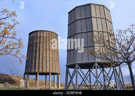 View of two weathered, cylindrical towers, one smooth and one segmented, stand as relics against a pale sky, in Puertollano, Castile-La Mancha, Spain. Stock Photo