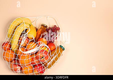 Lemons, oranges, tomatoes, apples, bananas, grapes and natural juice in a reusable bag, Fabric string bag with healthy vegan pro Stock Photo