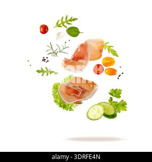 Traditional spanish jamon slices (dried pork meat) and fresh herbs and vegetables flying falling isolated on white background Stock Photo