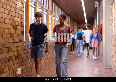 Walking in school hallway, students with backpacks talking and smiling Stock Photo