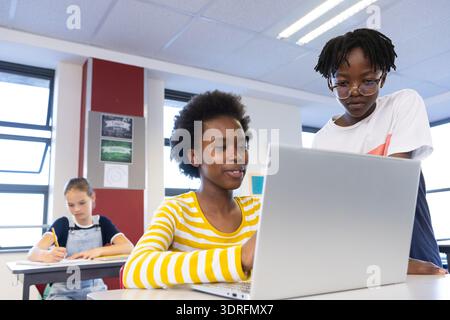 In school, diverse students collaborating on laptop while classmate writing in notebook Stock Photo