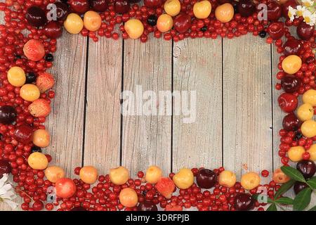 Frame of fresh red currant berries, cherries and cherries, top view, copy space. Red currant and sweet cherry on a wooden light Stock Photo