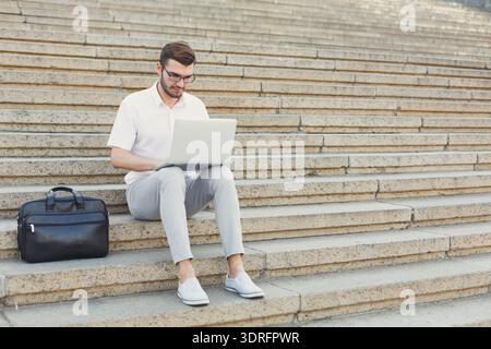 Man Works on Laptop While Sitting on Steps During Daytime in an Urban Setting Stock Photo