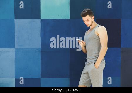 Young Man Checking Phone Against a Colorful Wall in Daytime Stock Photo