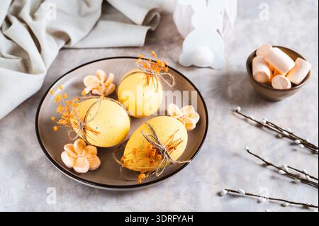 Easter eggs decorated with dried flowers and marshmallows on a plate on a table Stock Photo