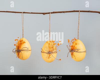 Three Easter eggs with dried flowers for decoration hanging on a branch on a gray background Stock Photo