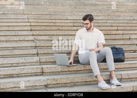Man Sitting on Steps Working on Laptop and Reviewing Documents During the Day Stock Photo