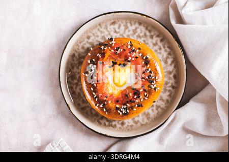 Close up of baked bagel with tomato and quail egg on a plate on the table top view Stock Photo