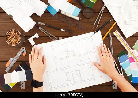 Hands Working on a Layout Plan With Various Colors and Tools Spread on a Wooden Table Stock Photo
