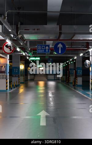 Underground parking garage with directional signs, green arrows on floor, illuminated ceiling, T2 section, Chinese exit signage Stock Photo
