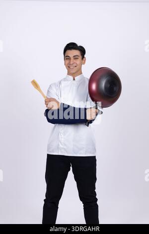 Young chef in uniform holding a frying pan in studio Stock Photo