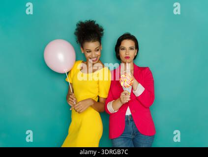 Two Women Pose With a Balloon and a Lollipop in Front of a Bright Background During Daytime Stock Photo