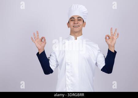 Smiling young chef in white uniform showing ok sign Stock Photo