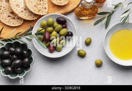 Bowls with green and black olives, olive oil and sliced bread on a wooden cutting board Stock Photo