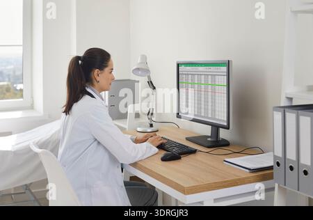 Doctor reviewing spreadsheet of medical records on computer in clinic office Stock Photo