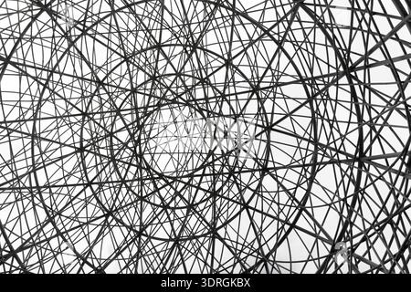 Abstract geometric structure of interwoven metal rods forming circular pattern against sky Stock Photo