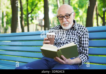 Senior Man Enjoys Reading a Book While Drinking Coffee in a Park During Daytime Hours Stock Photo