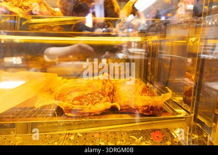 Spanish Jamón Serrano displayed in glass case at market stall, golden cured meat with marbled fat, warm lighting, European food tradition Stock Photo