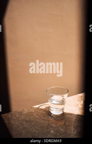 Close-up of a glass of clean water on a marble table. Transparent cup with water on a beige textured background. Stock Photo