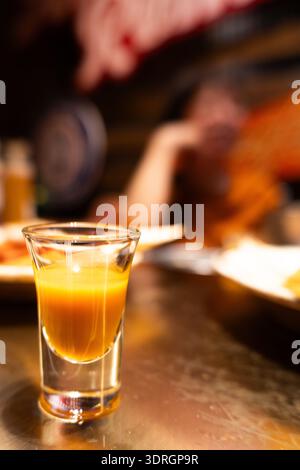 Orange shot glass filled with liquid on wooden bar table in dimly lit restaurant Stock Photo