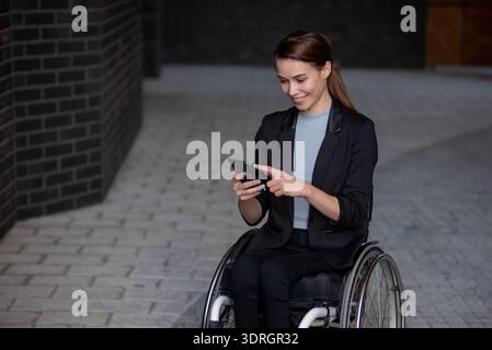Smiling businesswoman in wheelchair using smart phone outside Stock Photo