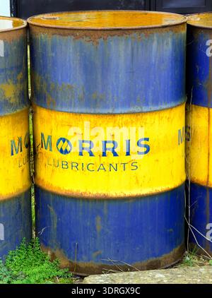 Close up of old, rusty metal industrial oil drums painted bright yellow and deep blue with 'MORRIS LUBRICANTS' text Stock Photo