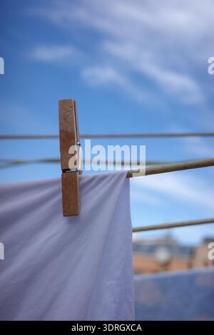 Wooden clothespin holding white laundry on clothesline against blue sky Stock Photo