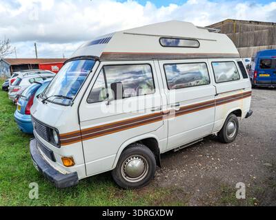 Vintage white Volkswagen T3 camper van with brown stripes parked outdoors next to other vehicles Stock Photo