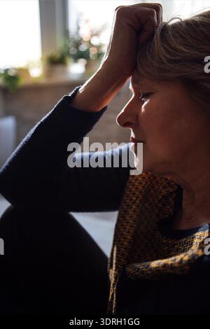Close-up of an elderly woman suffering from a headache. A mature lady is sitting on the floor and holding her forehead with her Stock Photo