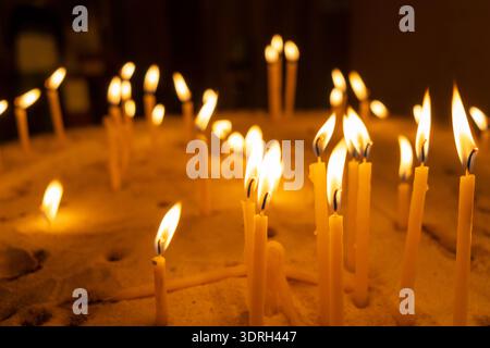 Burning candles with warm flames placed in a bed of sand Stock Photo