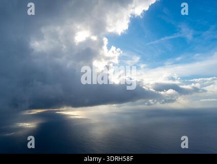 Majestic clouds illuminated by the sun create a dramatic sky viewed from above. The bright sunlight contrasts with the deep blue Stock Photo