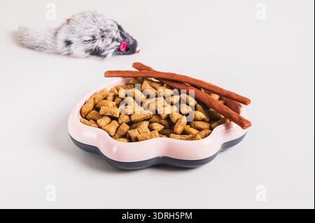 Bowl with dry cat food pellets and toy fluffy mouse on table Stock Photo
