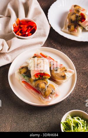 Delicious spring rolls with vegetables and mushrooms in rice paper on a plate vertical view Stock Photo