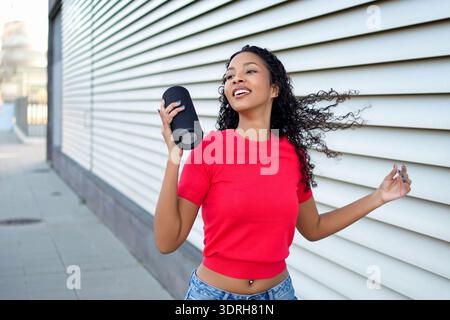 Energetic young woman with flowing hair performing dance in vibrant city scene with metal background Stock Photo