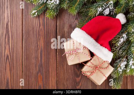 Christmas tree branch and santa hat with gift boxes on wooden table. Top view with copy space Stock Photo